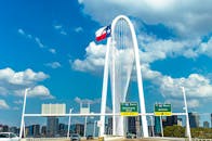 Iconic view of Margaret Hunt Hill Bridge with Texas flag and Dallas skyline under a blue sky.