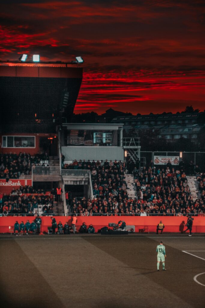 A vibrant soccer match in a stadium with spectators and a stunning sunset backdrop.