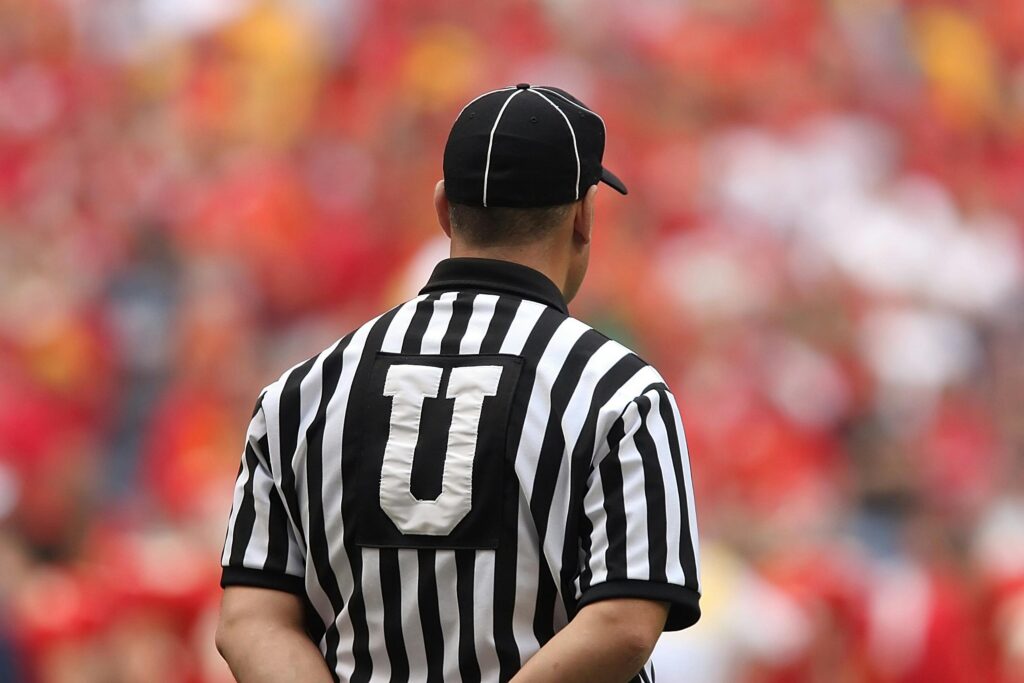 A football umpire in uniform overseeing the game in a crowded stadium.