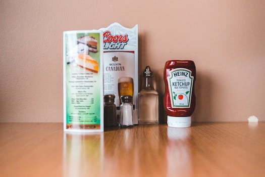 Kraft Heinz and NFL Announce Partnership Close-up of a restaurant table with ketchup, salt, pepper, and a menu on a wooden surface.