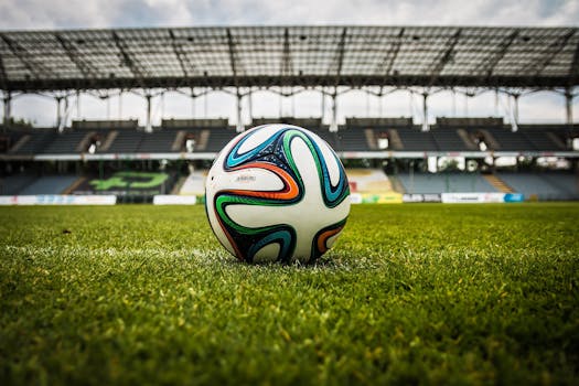 A vibrant soccer ball rests on a lush green field inside an empty stadium, capturing the essence of sports.