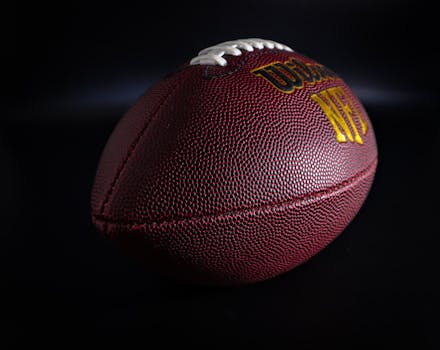 Detailed view of a traditional brown and white American football against a dark backdrop, highlighting texture.