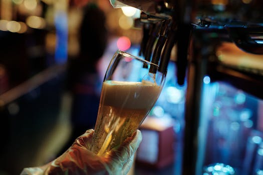 Close-up of a foamy beer being poured from a tap in a dimly lit bar setting.
