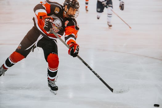 Relationship Between Draft Number and Current Salary (2019 NHL Draft) A male ice hockey player in full gear skates aggressively on ice during a game.